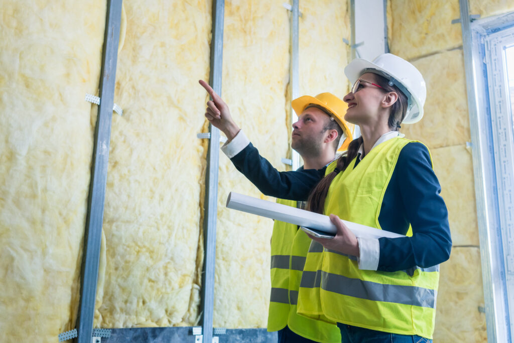 Construction workers inspect wall insulation. Yellow fiberglass insulation between metal studs. Building energy efficiency.